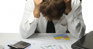 Homem de cabeça baixa com as mãos no rosto olhando boletos de dívidas