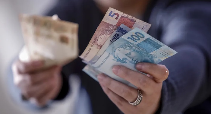 uma mão segurando notas de reais