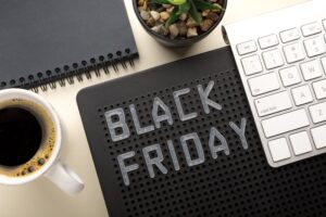 mesa com computador, xícara de café, caderno de anotações e placa de Black Friday