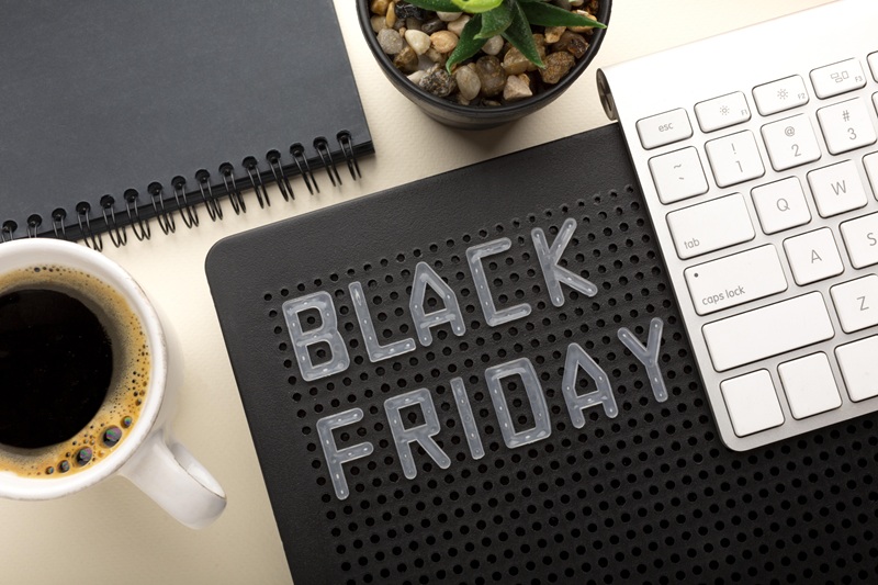 mesa com computador, xícara de café, caderno de anotações e placa de Black Friday