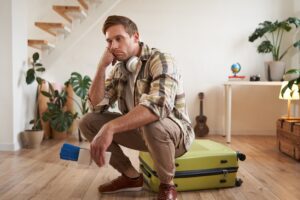 homem sentado sobre a mala com cara de decepção