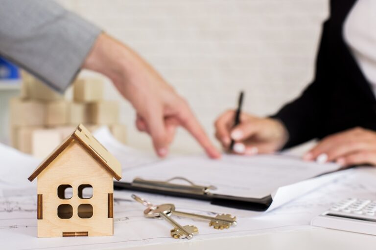 pessoa assinando contrato ao lado de uma miniatura de casa