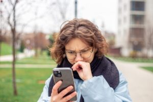 mulher de óclos olha o celular e sua expressão é de preocupação