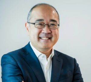 Ricardo Morishita está de camisa branca e paletó azul, óculos e sorrindo