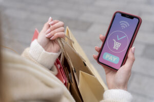 Mulher olhando celular para compras e com sacolas na mão