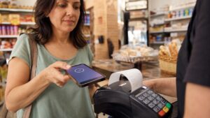 Mulher pagando conta da padaria com o celular e da máquina saindo a nota fiscal